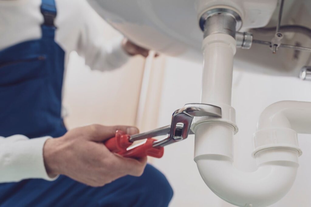 Plumber repairing a white drain pipe beneath a sink in Golden