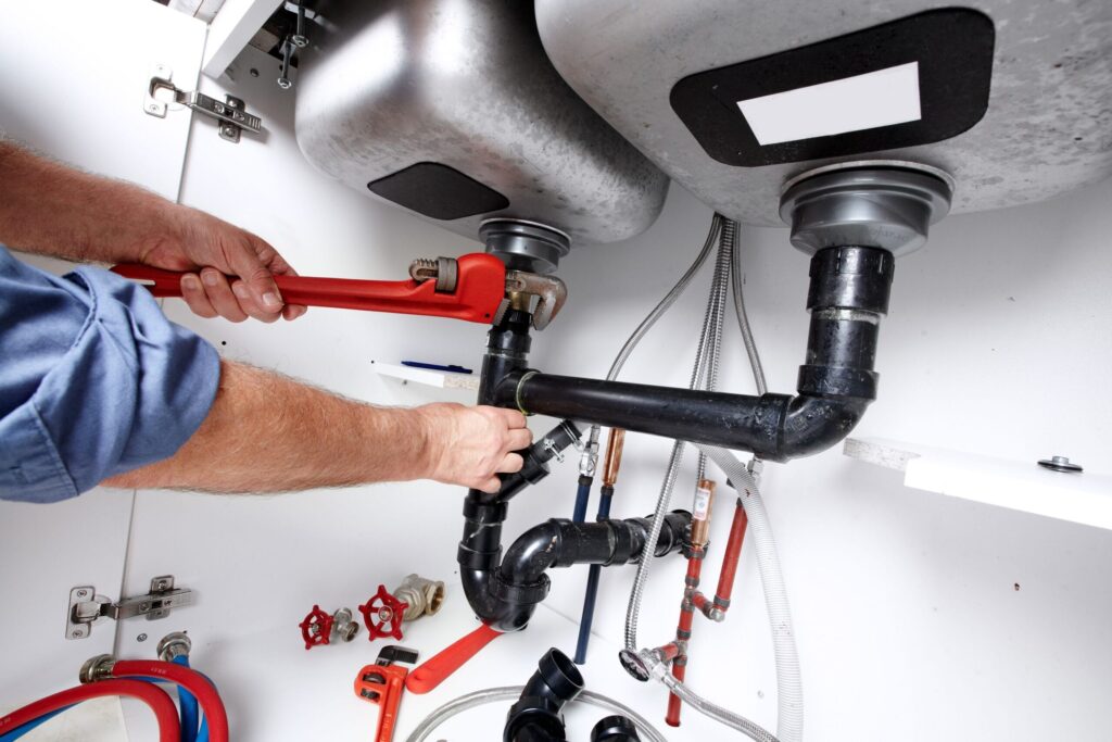 Plumber repairing drain pipes beneath a kitchen sink in Golden